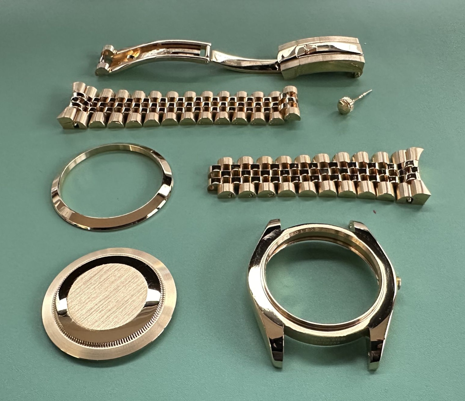 A Rolex fully disassembled on the bench: clasp, two bracelet halves, bezel, case-back, case and crown, freshly gold-plated
